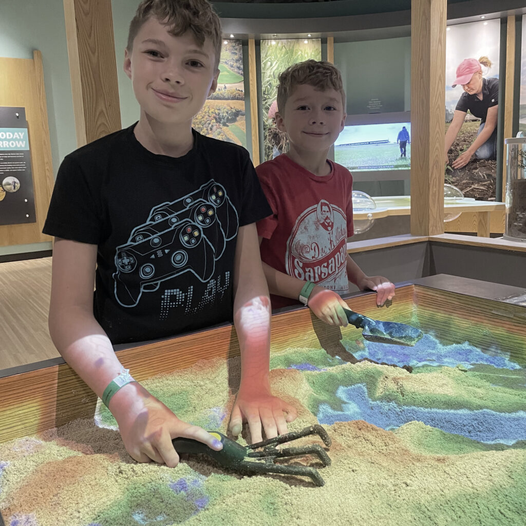 Two young male students smiling by the kinetic sand table